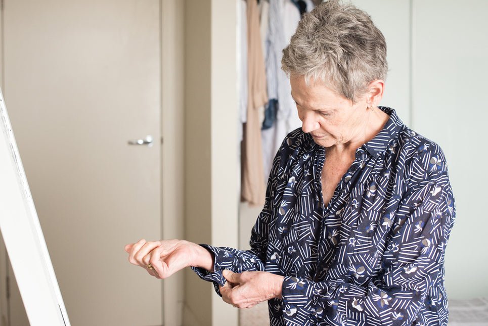 an elderly woman buttoning the cuffs on her shirt