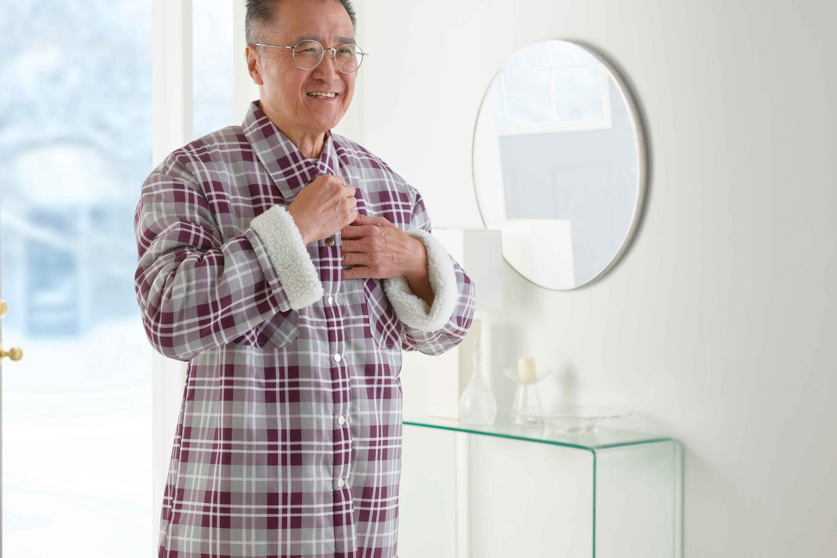 Older man standing in home front hall doing up jacket.
