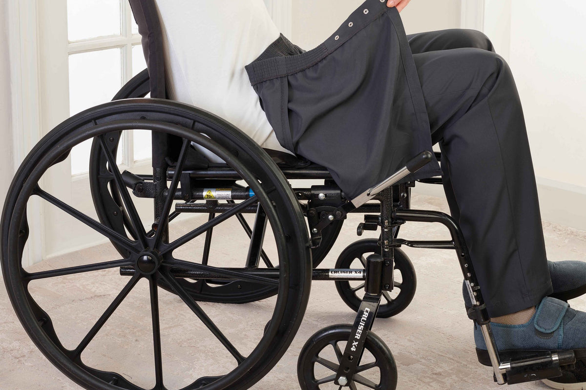 Side view of man seated in wheelchair with open back pants being put on.