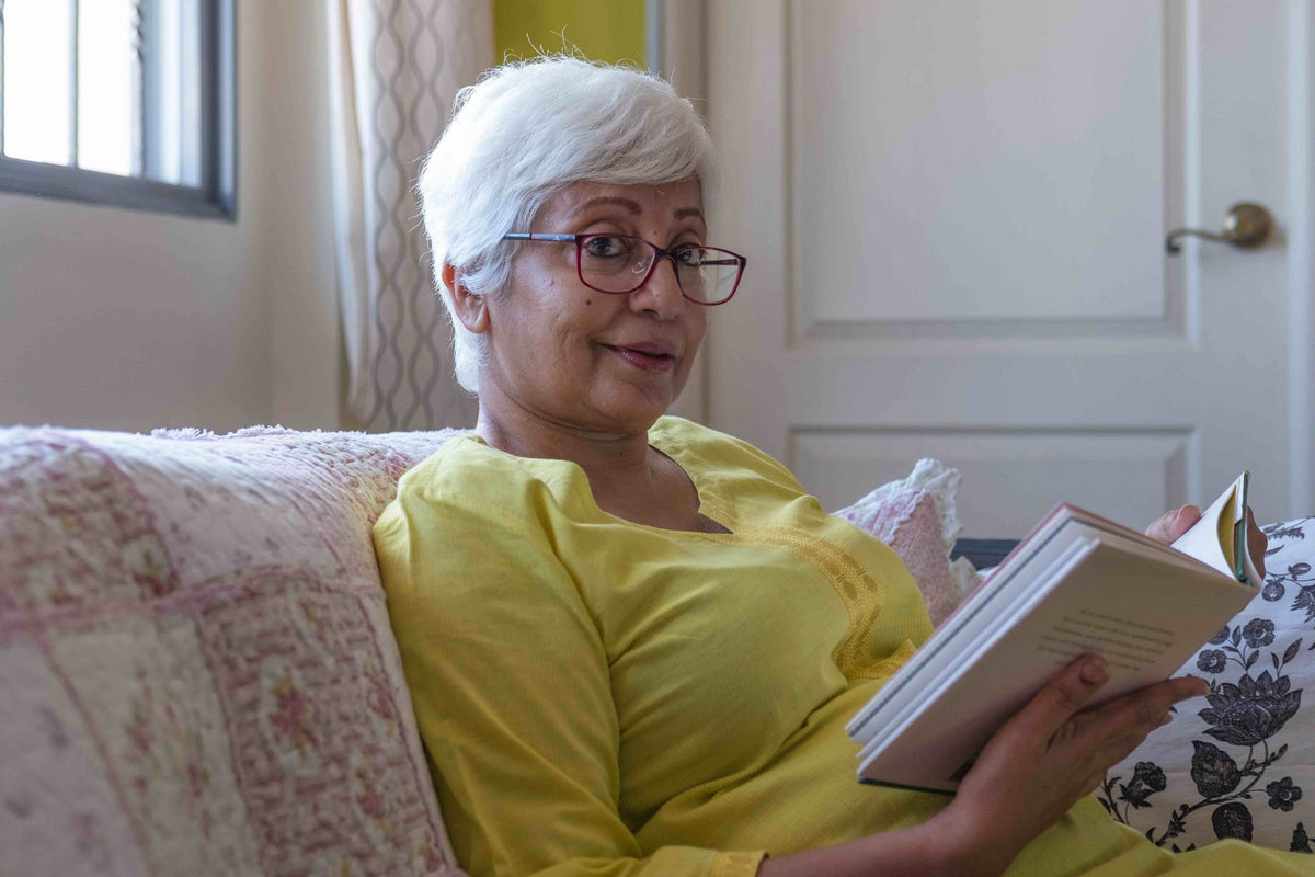 Middle aged women reading a book from the comfort of a couch.