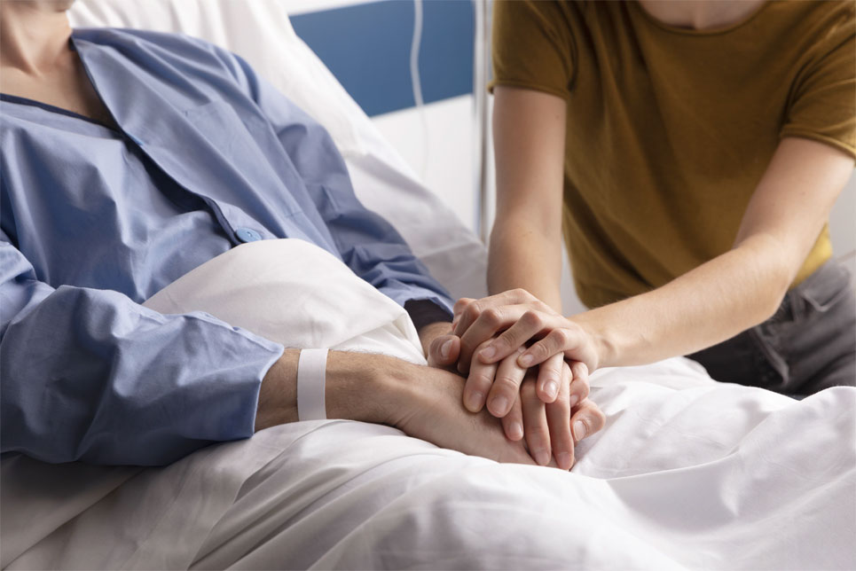 A man in a hospital bed holds hands with a woman beside him.